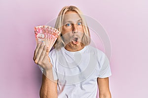 Caucasian young man with long hair holding 50 philippine peso banknotes scared and amazed with open mouth for surprise, disbelief