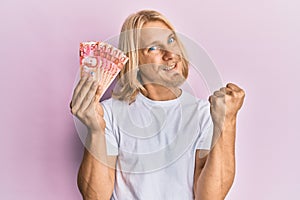 Caucasian young man with long hair holding 50 philippine peso banknotes screaming proud, celebrating victory and success very