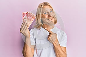 Caucasian young man with long hair holding 50 philippine peso banknotes smiling happy pointing with hand and finger