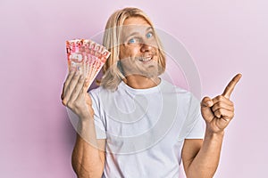 Caucasian young man with long hair holding 50 philippine peso banknotes smiling happy pointing with hand and finger to the side