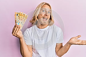 Caucasian young man with long hair holding 500 philippine peso banknotes celebrating achievement with happy smile and winner