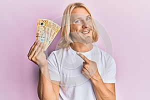 Caucasian young man with long hair holding 500 philippine peso banknotes smiling happy pointing with hand and finger