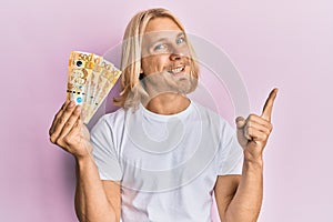 Caucasian young man with long hair holding 500 philippine peso banknotes smiling happy pointing with hand and finger to the side