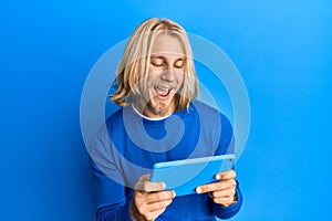 Caucasian young man with long hair using touchpad device smiling and laughing hard out loud because funny crazy joke