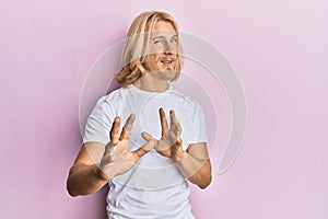 Caucasian young man with long hair wearing casual white t shirt disgusted expression, displeased and fearful doing disgust face