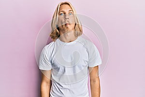 Caucasian young man with long hair wearing casual white t shirt making fish face with lips, crazy and comical gesture