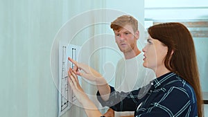 Caucasian young man and woman in new house looking at plan of the flat and using measuring tape. Close up. Family couple