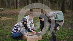 Caucasian young man and women caressing cute puppy in paper box in summer park. Wide shot positive volunteers searching