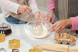 Caucasian young mother and little daughter in aprons make dough for cookies with whisk, have fun in kitchen