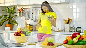 Caucasian young pregnant female mother in casual outfit with big belly tummy standing smiling holding vegetarian salad bowl eating