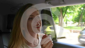 Caucasian young pretty blonde woman sitting in auto holding smartphone and telling the direction to a driver. Taxi drive