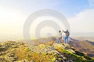 Caucasian young travelous couple enjoy mountain top viewpoint panorama together after reaching top. Hands up clapping for success