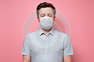 Caucasian young unemotional man wearing medical mask standing with closed eyes