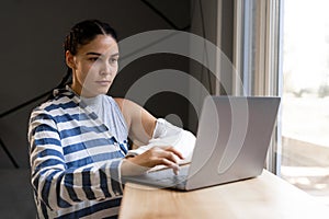Caucasian young woman with broken arm typing on the laptop in cafe after a having an accident and a broken bone