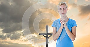 Caucasian young woman with closed eyes praying while standing against silhouette cross during sunset