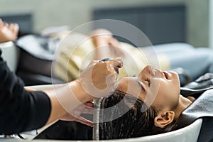 Caucasian young woman get hair washed by Hairdresser stylist in salon. Beautiful customer girl lying down on salon washing bed