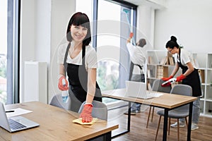 Caucasian young woman holding sponge and detergent cleaning on table in office.