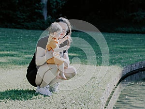 Caucasian young woman mother holding her baby girl gently looking at her n a public park