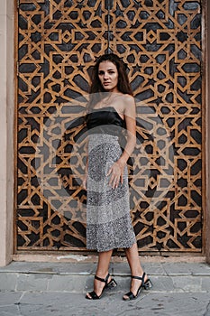 Caucasian young woman posing at a wooden door in Arabic style. Oriental style