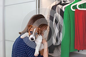 Caucasian young woman with a puppy in her hands puts clothes in the closet.