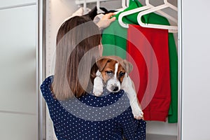 Caucasian young woman with a puppy in her hands puts clothes in the closet.