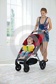 Caucasian young woman pushing stroller with toddler boy indoors