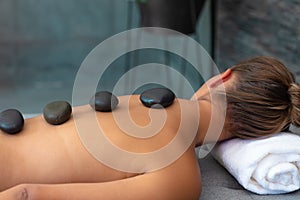 Caucasian young woman receiving hot stone massage lying on the massage table