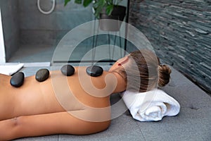 Caucasian young woman receiving hot stone massage lying on the massage table