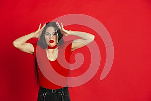 Caucasian young woman`s monochrome portrait on red studio background, emotional and expressive