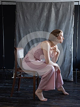 Caucasian young woman with short hair in pink suit sitting on chair in studio