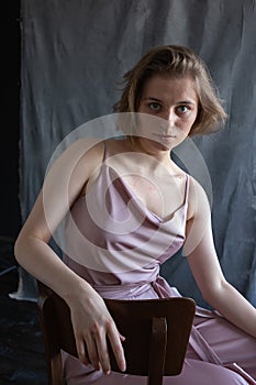 Caucasian young woman with short hair in pink suit sitting on chair in studio