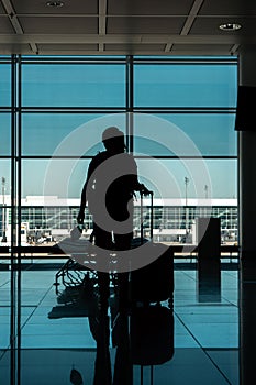 Caucasian young woman silhouette standing in an empty international airport terminal gate with a face mask in her hand next to her