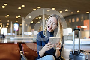 Caucasian young woman sitting in airport waiting room with valise and using tablet.