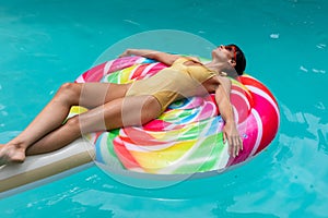 Caucasian young woman in swimwear relaxing on inflatable ring in swimming pool