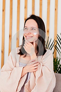 Caucasian young woman touching face and applying cream indoors. Morning beauty routine. Skincare concept