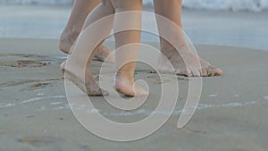 Caucasian young woman and two years old baby playing on sunset beach. Close-up of mom and daughter legs standing near