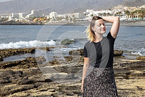 Caucasian young woman wearing a neutral outfit and relaxing at Playa de Las Americas, with the entire Costa Adeje visible