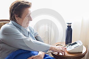 Caucasic woman over 70 checking her blood pressure at home with a digital monitor. Short hair  blue sweater