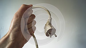 A caucassian male hand holding a electric plug unplugged against a white background