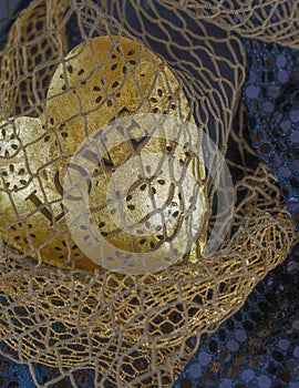 Caught in a golden fish net is a metal dimensional heart with floral cutouts. Behold a capture at sea.