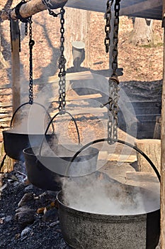 Cauldrons steaming over an open fire concentrating maple syrup slowly