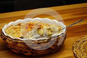 Cauliflower with bechamel sauce and melted cheese on top in ceramic dish with straw mat cover