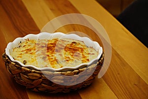 Cauliflower with bechamel sauce and melted cheese on top in ceramic dish with straw mat cover