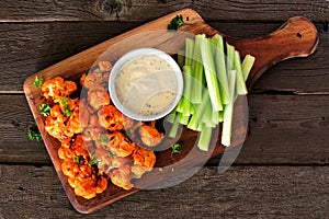 Healthy vegan cauliflower buffalo wings with celery and ranch dip, top view on a wood paddle board photo