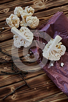 cauliflower pieces on wooden table and purple craft paper