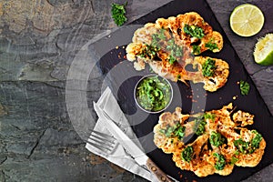 Cauliflower steaks top view scene on a dark background, healthy plant based meat substitute concept