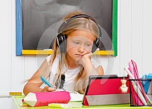 Causacian cute school kid with earphones is on boring online home education. Distance learning