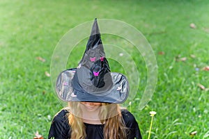 Causcasian blond girl with long hair in halloween witch costume sitting on a grass