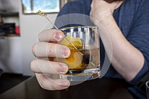 a causcasian male hand holding an old fashioned alcoholic drink inside of a bar and restaurant