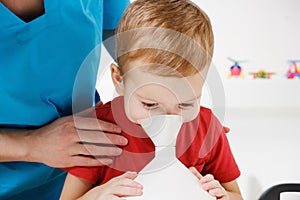 Causian little boy making inhalation with nebulizer at hospital.